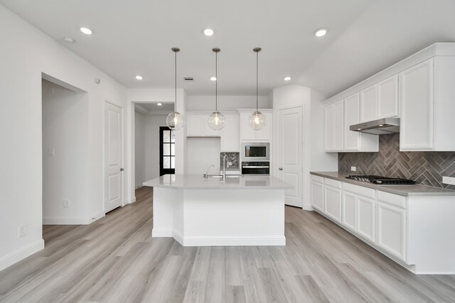 kitchen featuring appliances with stainless steel finishes, a center island with sink, pendant lighting, and light hardwood / wood-style flooring