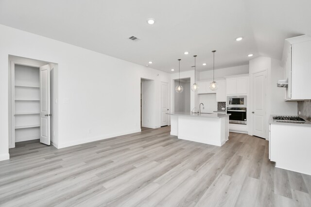 kitchen featuring appliances with stainless steel finishes, an island with sink, white cabinets, pendant lighting, and light hardwood / wood-style flooring