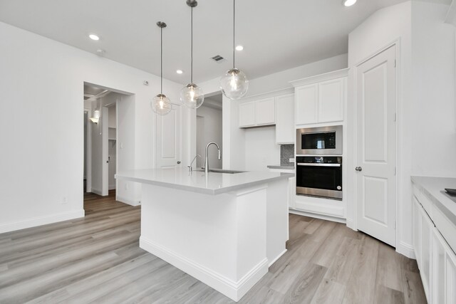 kitchen featuring sink, decorative light fixtures, a center island with sink, white cabinetry, and appliances with stainless steel finishes