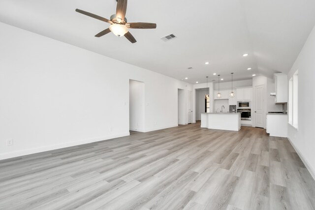 unfurnished living room featuring light wood-type flooring, ceiling fan, and sink