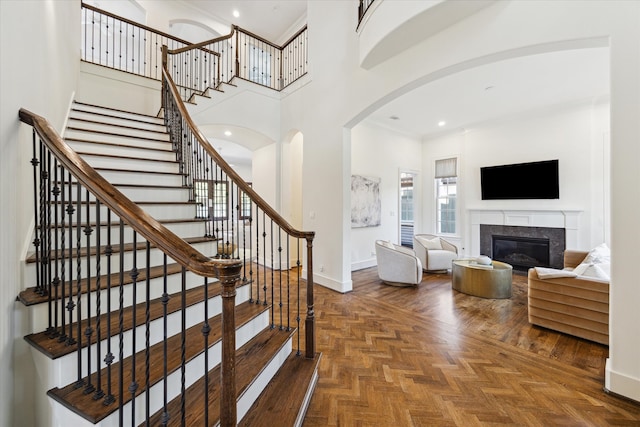 stairway with a high ceiling, a fireplace, and parquet floors