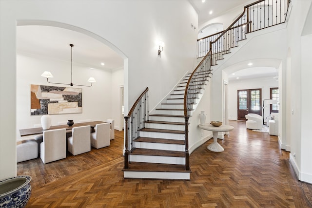 stairway featuring a towering ceiling, crown molding, and parquet floors