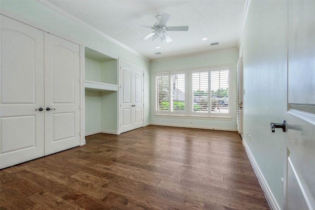 unfurnished bedroom featuring ceiling fan, multiple closets, crown molding, and dark wood-type flooring