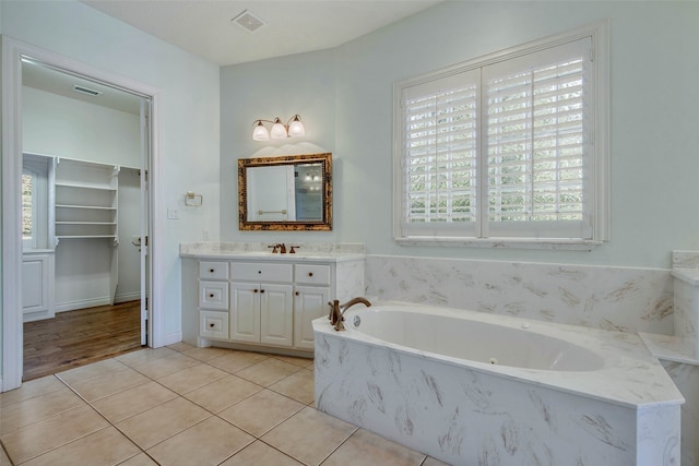 bathroom with a relaxing tiled tub, vanity, and tile patterned flooring