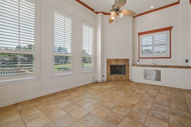 unfurnished living room with ceiling fan, a tile fireplace, a healthy amount of sunlight, and crown molding