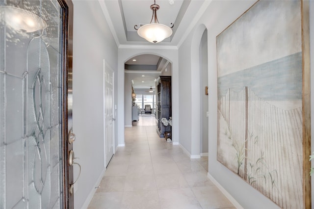 hallway featuring light tile patterned floors, ornamental molding, and a tray ceiling