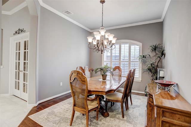 dining area with french doors, light hardwood / wood-style floors, crown molding, and an inviting chandelier