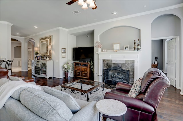 living room featuring ceiling fan, ornamental molding, a tile fireplace, and dark hardwood / wood-style floors