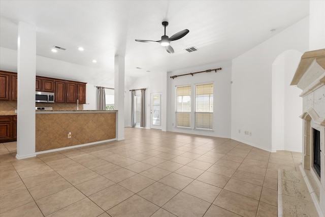 unfurnished living room featuring ceiling fan, light tile patterned floors, a healthy amount of sunlight, and a tiled fireplace