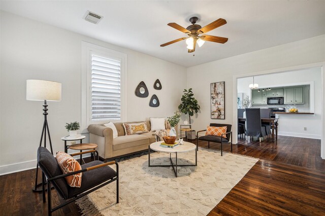 living area featuring baseboards, visible vents, dark wood-style flooring, and ceiling fan with notable chandelier