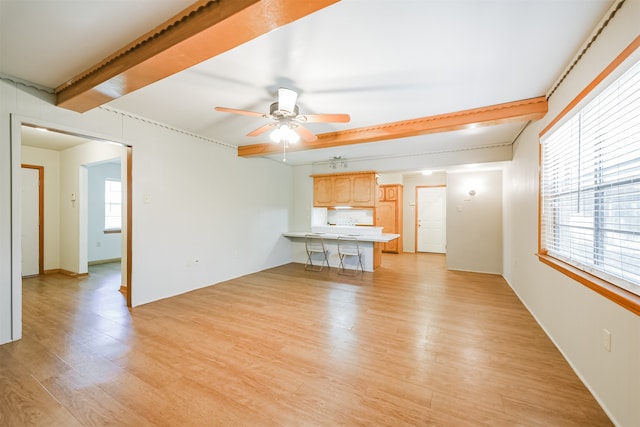 unfurnished living room featuring beamed ceiling, ceiling fan, and light hardwood / wood-style flooring