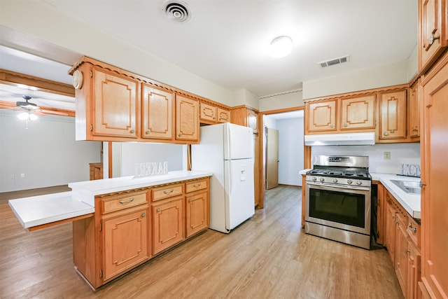 kitchen featuring ceiling fan, white refrigerator, kitchen peninsula, stainless steel gas stove, and light wood-type flooring