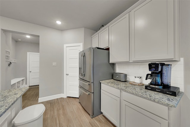 kitchen featuring stainless steel refrigerator, white cabinetry, light stone counters, decorative backsplash, and light wood-type flooring