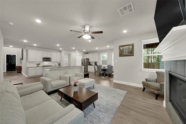 living room featuring a tile fireplace, ceiling fan, and light wood-type flooring