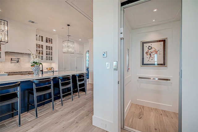 kitchen featuring decorative backsplash, light wood-type flooring, decorative light fixtures, white cabinetry, and a breakfast bar area