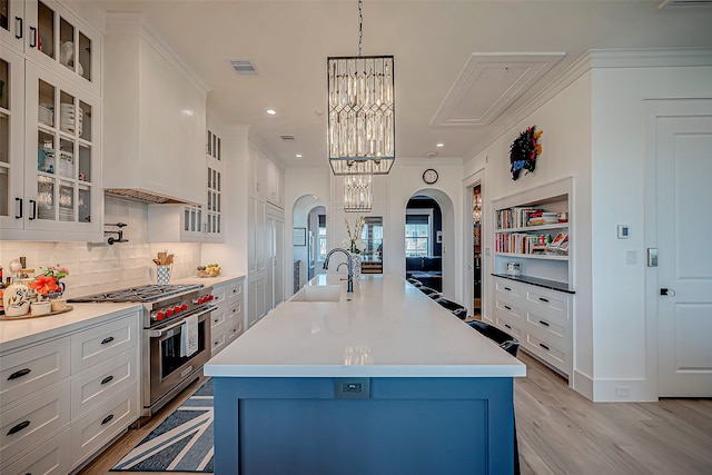 kitchen featuring hanging light fixtures, a center island with sink, double oven range, and light hardwood / wood-style floors