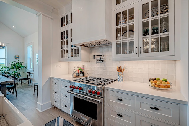 kitchen with decorative backsplash, custom range hood, vaulted ceiling, luxury stove, and white cabinets