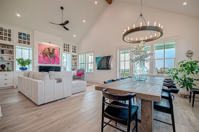 dining space featuring beamed ceiling, light hardwood / wood-style floors, high vaulted ceiling, and an inviting chandelier