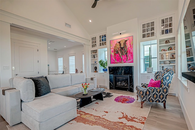 living room featuring a fireplace, high vaulted ceiling, light hardwood / wood-style flooring, and built in features