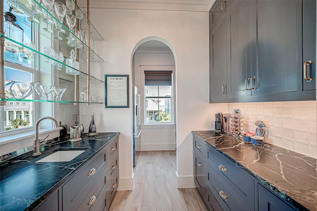 bar featuring dark stone counters, light hardwood / wood-style floors, a healthy amount of sunlight, and sink