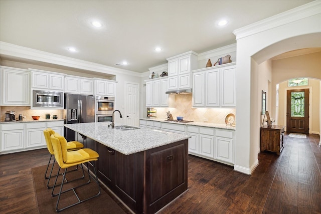kitchen with stainless steel appliances, arched walkways, a sink, and white cabinetry