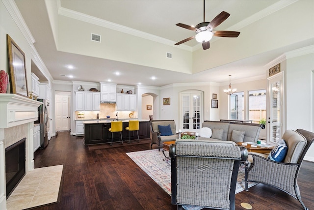 living area featuring arched walkways, a tiled fireplace, visible vents, and dark wood-style floors