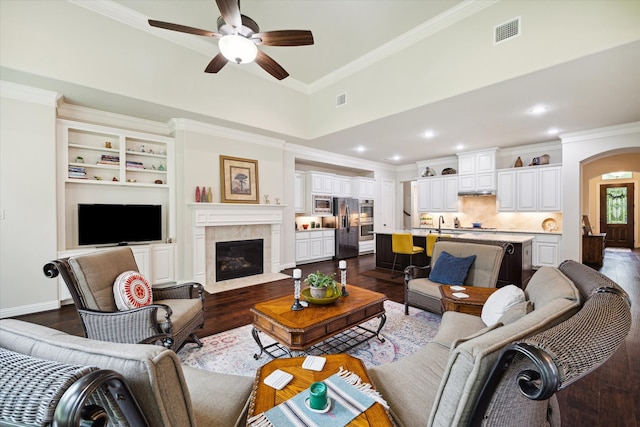 living room featuring ceiling fan, a tiled fireplace, dark hardwood / wood-style floors, and crown molding