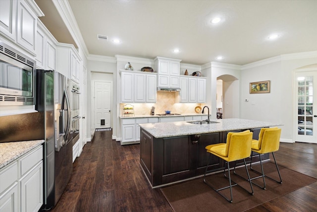 kitchen featuring stainless steel appliances, visible vents, a sink, arched walkways, and decorative backsplash