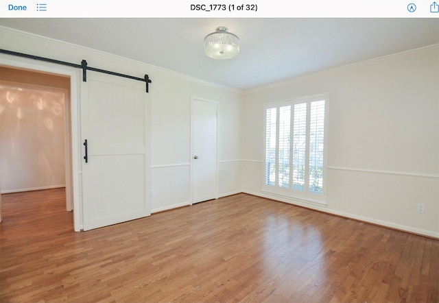 unfurnished bedroom featuring ornamental molding, a barn door, and light hardwood / wood-style floors