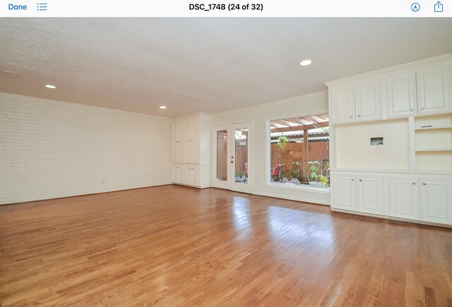 unfurnished living room with brick wall and light wood-type flooring