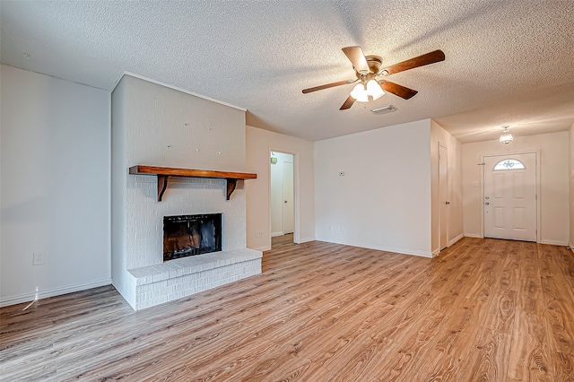 unfurnished living room with a textured ceiling, ceiling fan, light wood-type flooring, and a brick fireplace