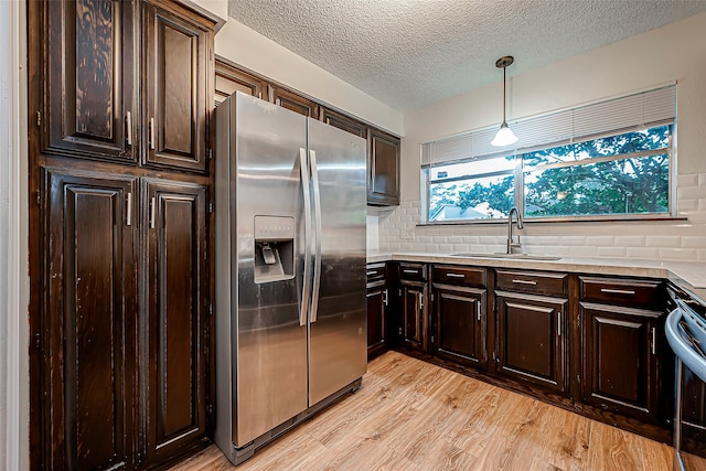 kitchen with stainless steel fridge, light wood-type flooring, black range oven, decorative light fixtures, and sink