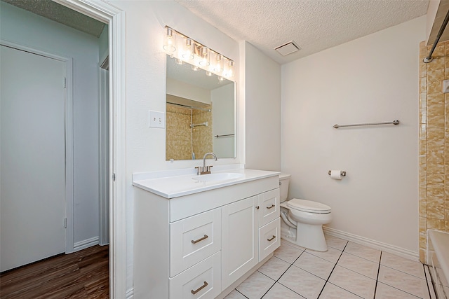 full bathroom with a textured ceiling, toilet, vanity, tiled shower / bath combo, and tile patterned floors