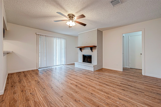 unfurnished living room featuring a brick fireplace, a textured ceiling, light hardwood / wood-style floors, and ceiling fan