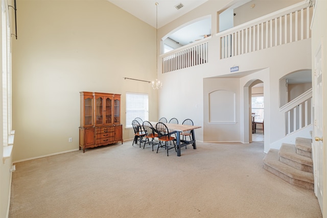 carpeted dining room with a towering ceiling, a healthy amount of sunlight, and a notable chandelier