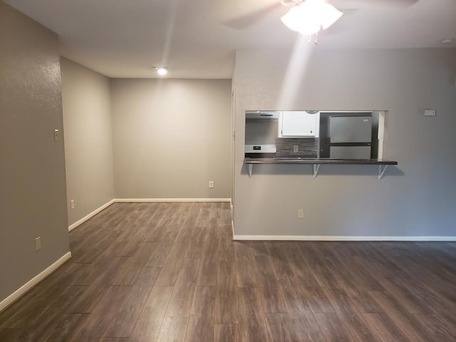 kitchen with dark hardwood / wood-style floors, a breakfast bar area, white cabinets, kitchen peninsula, and stainless steel refrigerator