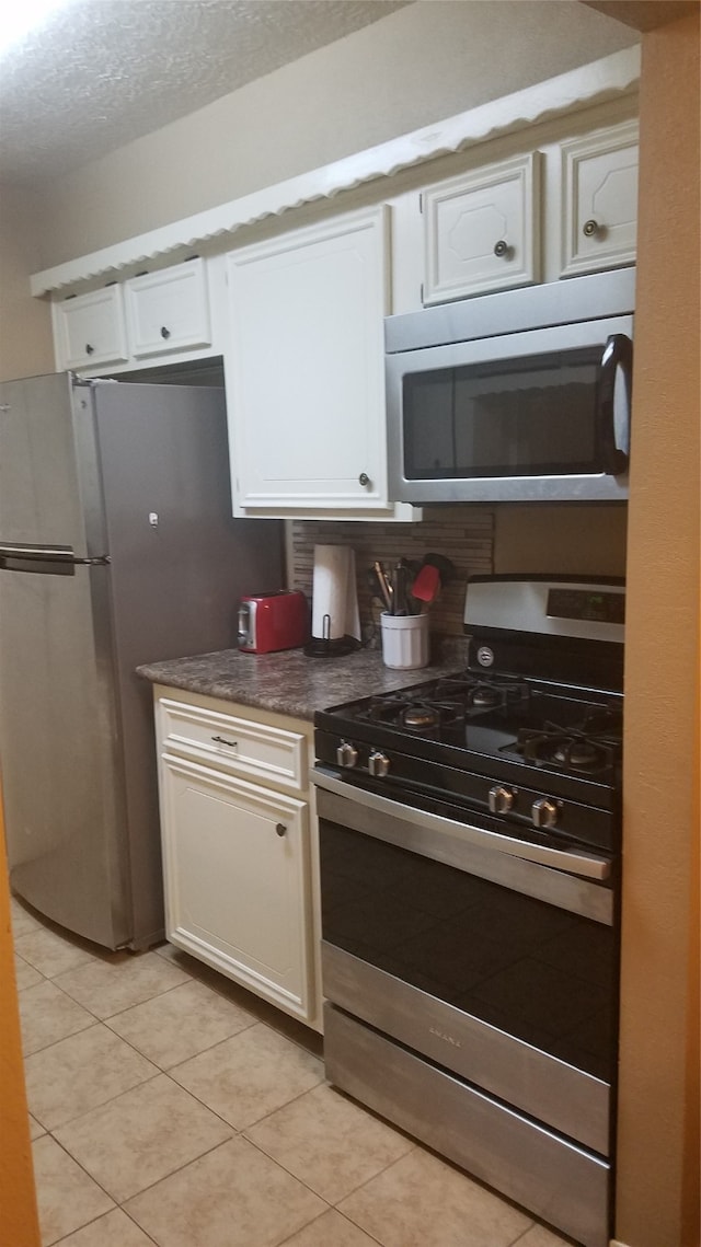 kitchen with appliances with stainless steel finishes, decorative backsplash, white cabinets, light tile patterned floors, and a textured ceiling