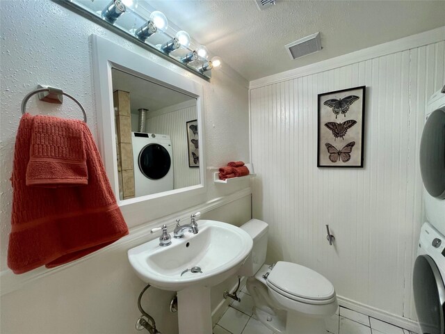 bathroom with visible vents, toilet, stacked washer / dryer, a textured ceiling, and tile patterned floors