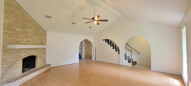 unfurnished living room with light hardwood / wood-style floors, high vaulted ceiling, a fireplace, beam ceiling, and ceiling fan