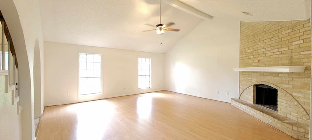 unfurnished living room with ceiling fan, a fireplace, beam ceiling, and light hardwood / wood-style floors