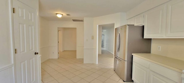 kitchen with stainless steel refrigerator, white cabinetry, and light tile patterned floors