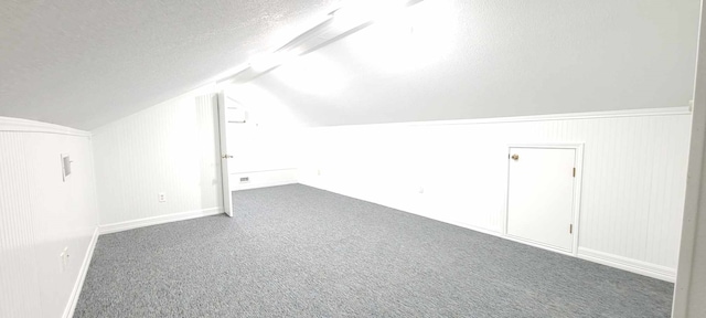 bonus room with dark carpet, lofted ceiling, and a textured ceiling