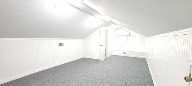 additional living space featuring a textured ceiling, lofted ceiling, and dark carpet