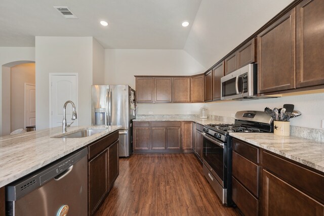 kitchen with appliances with stainless steel finishes, vaulted ceiling, light stone counters, dark hardwood / wood-style floors, and sink