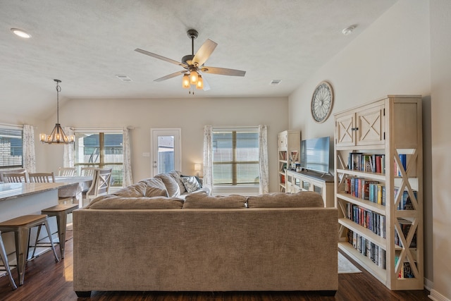 living room with a healthy amount of sunlight, ceiling fan with notable chandelier, vaulted ceiling, and dark wood-type flooring