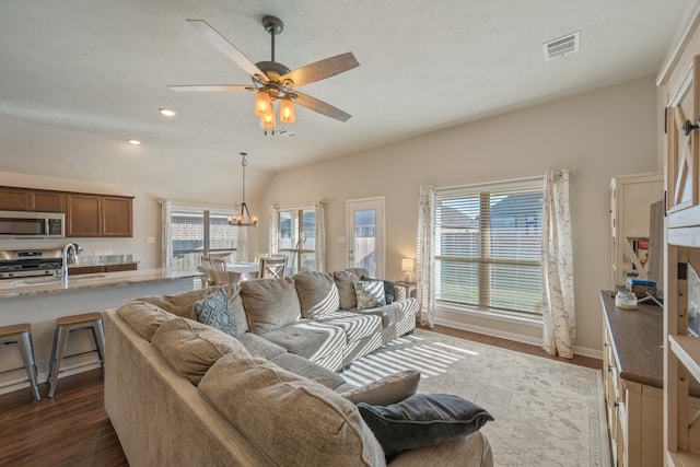 living room featuring ceiling fan with notable chandelier, vaulted ceiling, sink, and dark wood-type flooring