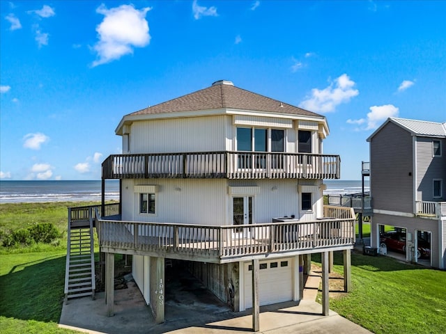 back of property featuring a garage, a view of the beach, a deck with water view, and a yard