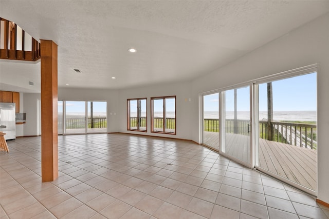 empty room featuring a water view, a textured ceiling, and light tile patterned flooring