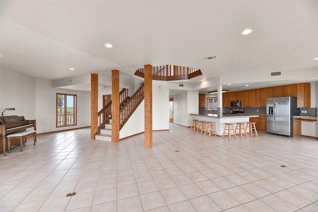 kitchen with a kitchen breakfast bar, brown cabinets, open floor plan, stainless steel appliances, and visible vents