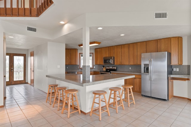 kitchen with a breakfast bar area, appliances with stainless steel finishes, tasteful backsplash, and light tile patterned flooring